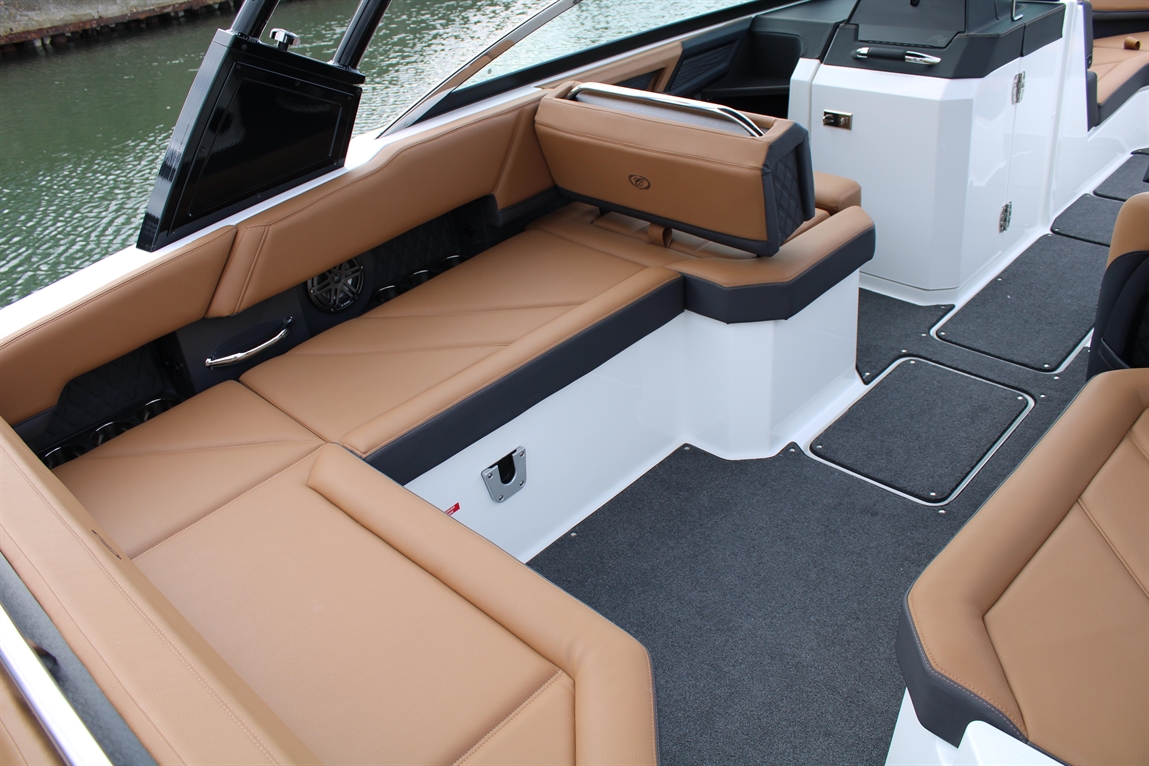 Luxury boat interior featuring tan leather seating, gray carpet, and a small monitor, against a water backdrop.